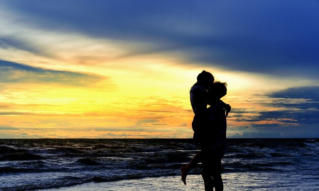 Man lifting girlfriend at beach during sunset