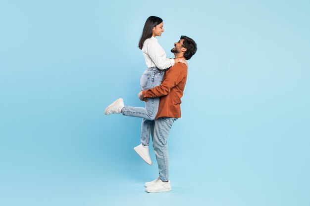 Man lifting woman on blue background in joyful pose