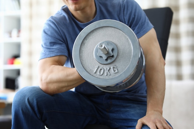 Man lifts heavy dumbbell while sitting on sofa