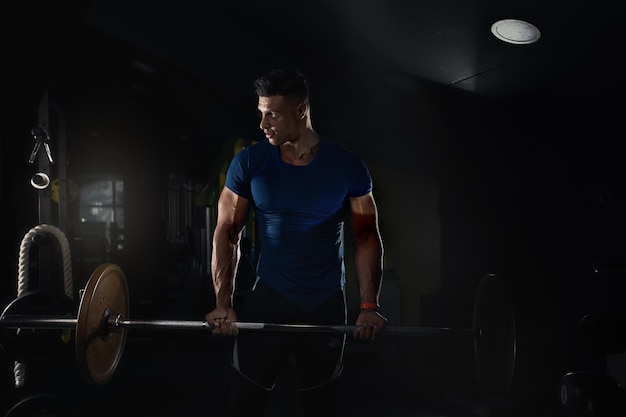 A man lifts weights in the gym and looks to the side in a tight tshirt creative photo