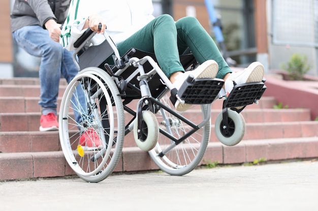 Photo man lifts wheelchair up steps with woman adaptation of stairs for disabled people concept