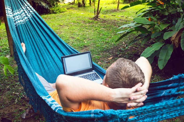 Man liggend in een hangmat en werken op een laptop in de tuin