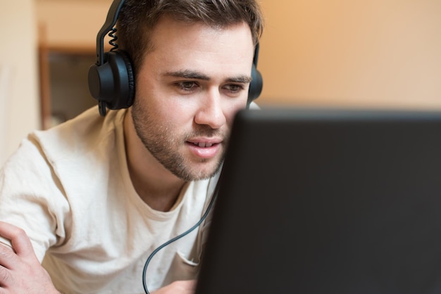 Man liggend op de vloer met koptelefoon op laptop