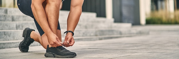 A man in a light athletic uniform ties a lace on a shoe for
running