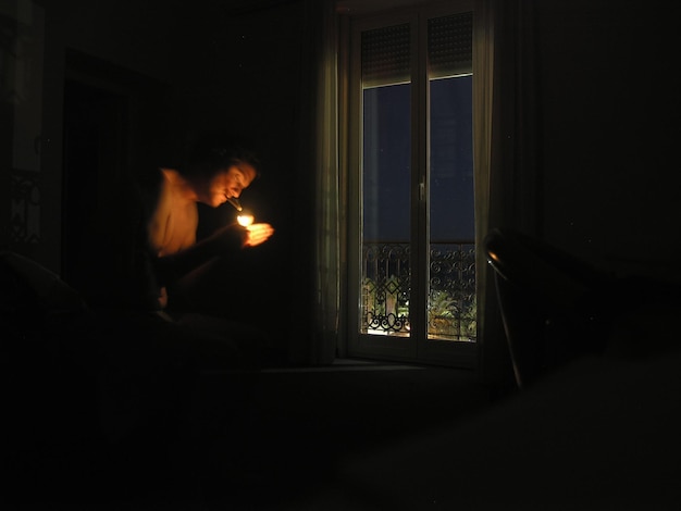 Photo man lighting a cigarette near the window