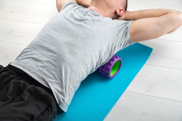 Man ligt op de myofasciale roller. Man voert myofasciale afgifte van hyperbeweegbare rugspieren uit met massageroller.