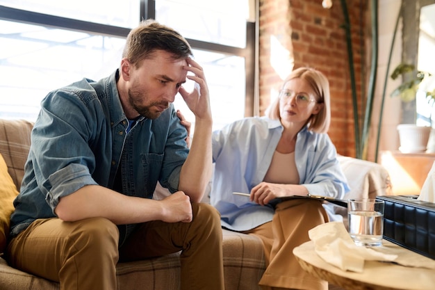 Photo man listening to advice of psychotherapist while sitting on sofa during his visit to psychologist of