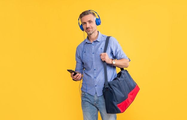 Man listening music in earphones chatting on phone hold sports bag on yellow background music