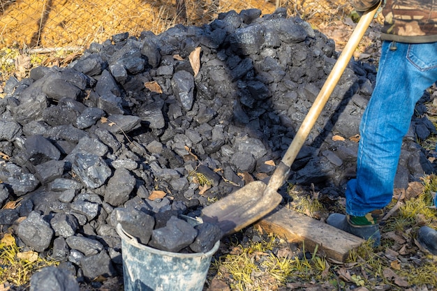 A man loads coal into a bucket with a shovel. Heating a country house during the cool season in autumn and winter.