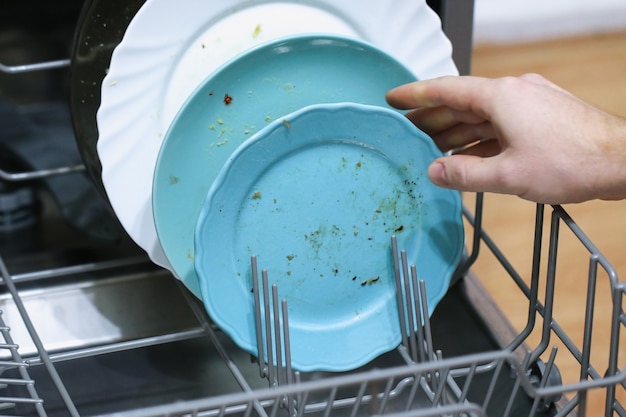 A man loads dirty dishes, plates, spoons, forks, cutlery into the dishwasher tray.