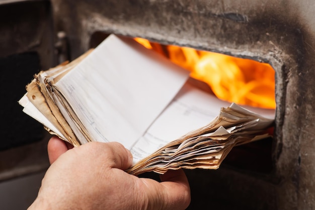 Man loads old paper in the solid fuel boiler heating in cold\
winter season keeping the fire in boiler and high temperature in\
system