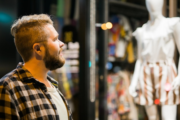 저녁 거리 상점에서 상점 창을 보고 있는 남자와 쇼핑 중독적인 소비주의 개념