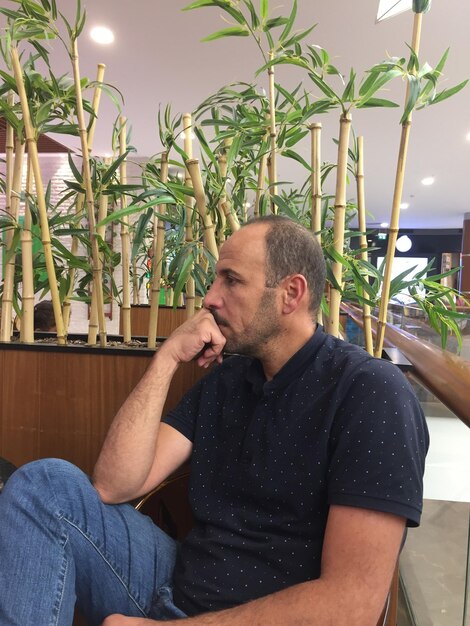 Foto uomo che guarda lontano mentre è seduto sul sedile vicino alle piante