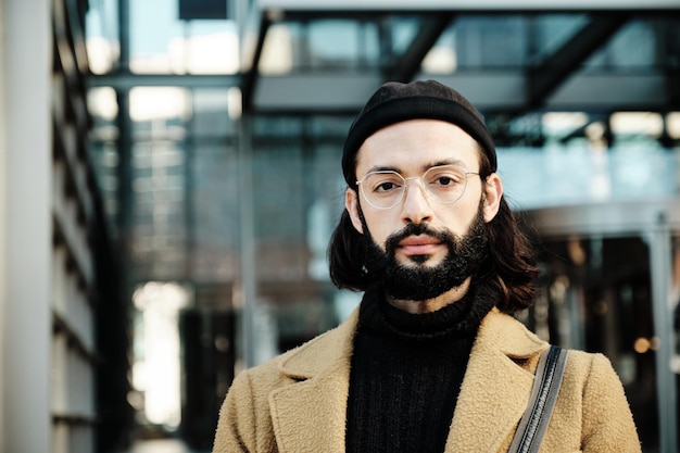 Man looking at the camera with a serious expression on his face while standing against an office building.