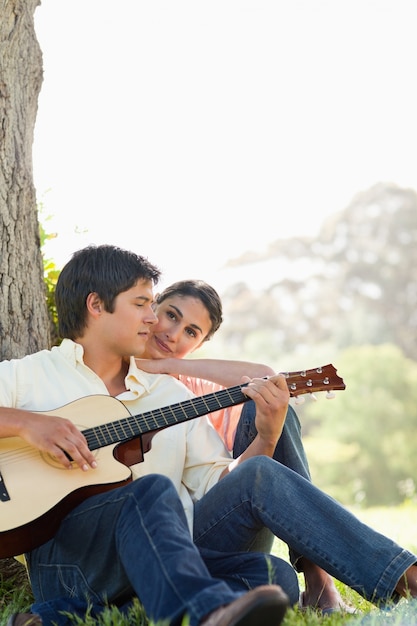 Man looking down while playing the guitar as his friend watches him