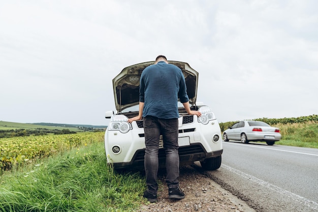 Man looking at engine at broken car at roadside