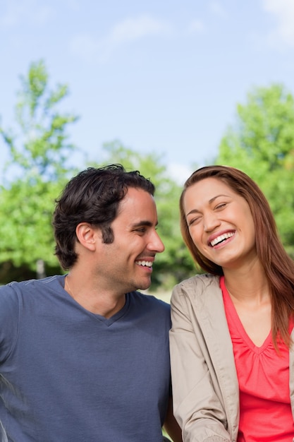 Man looking his friend as she is laughing joyfully while sitting in a park