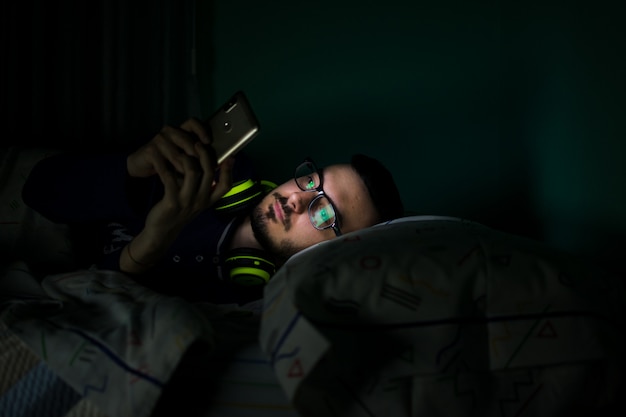 Uomo che guarda il suo telefono cellulare nel letto di notte