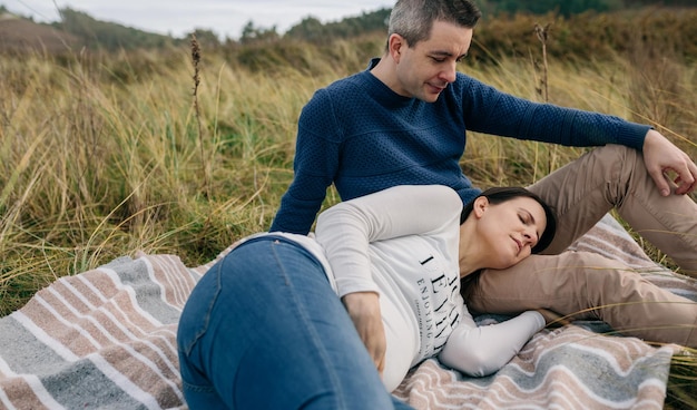 Man looking his pregnant woman resting on the grass