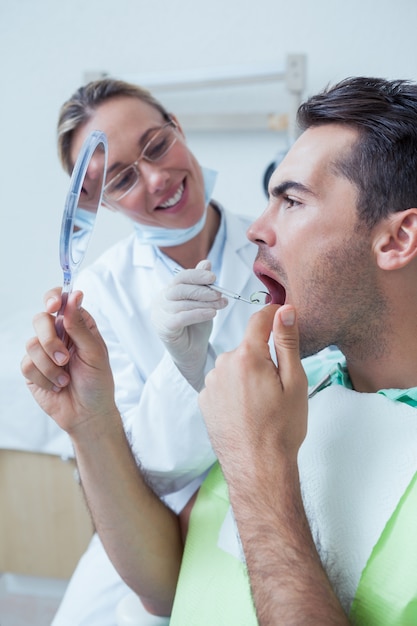 Foto uomo che guarda allo specchio dal dentista femminile