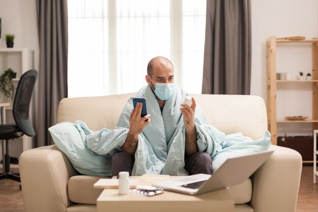 Man looking at pills bottle during a video call on smartphone with doctor.