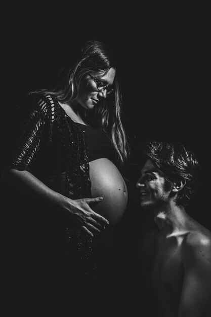 Man looking at pregnant woman belly against black background