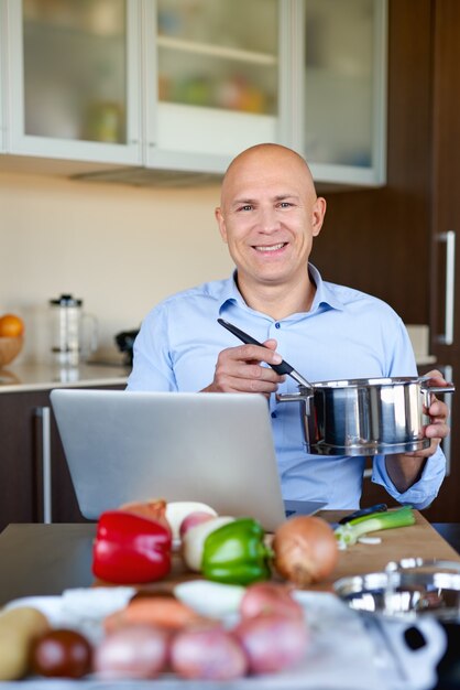 夕食を調理しながらノートパソコンでレシピを見ている男