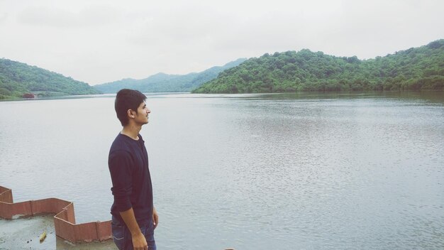 Man looking at river by mountains against sky