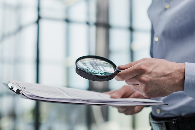 Photo man looking through a magnifying glass to documents notebook