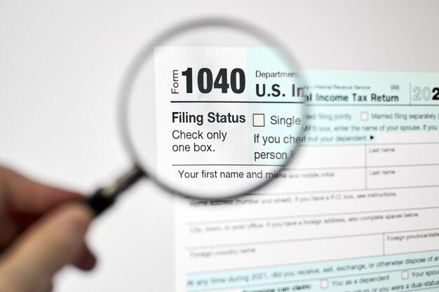 Man looking through a magnifying glass at US Individual Income Tax Return declaration form 1040