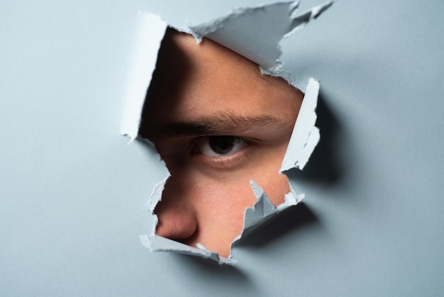 Man looking through paper A jealous husband Hole torn in paper with the eye of boy Portrait of man l