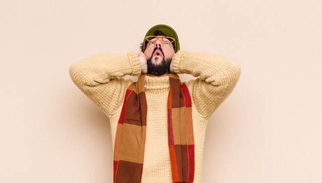 Man looking unpleasantly shocked, scared or worried, mouth wide open and covering both ears with hands