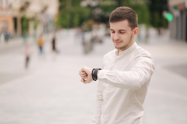 屋外で時計を見ている男 街で白いシャツを着た若い男