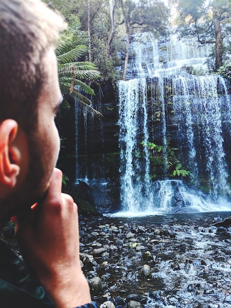 Foto uomo che guarda la cascata nella foresta