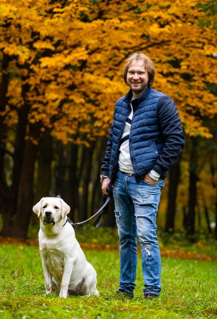 Man looks at camera while having a walk with retriver dog Fabulous atumn park in golden colors Full body portrait Closeup