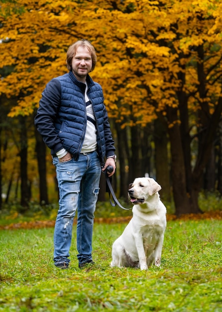 Man looks at camera while having a walk with retriver dog Fabulous autumn park in golden colors Full body portrait Closeup