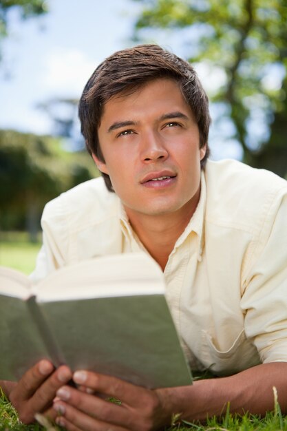 Man looks to the distance while reading a book as he is lying down