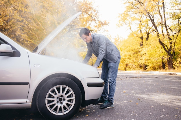 A man looks under the open hood of a car The car broke down on the road The engine is smoking