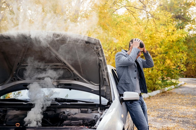 A man looks under the open hood of a car The car broke down on the road The engine is smoking