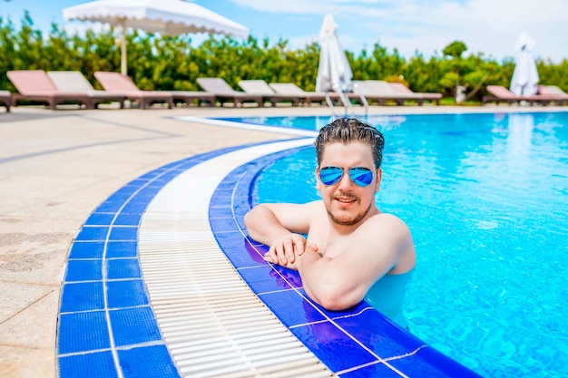 A man looks out of the pool, hanging on the railing.