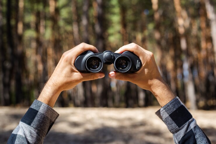 Photo man looks through binoculars against the of the forest.