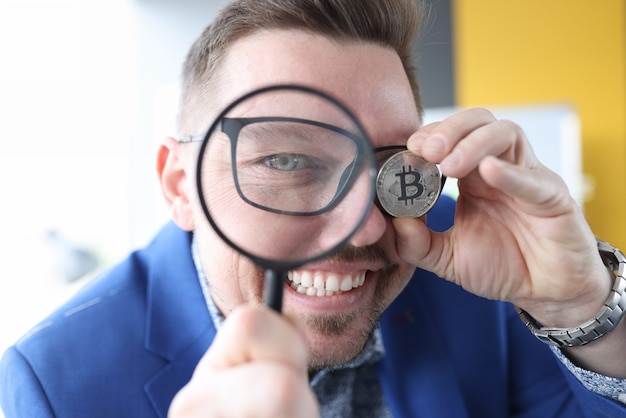 Man looks through magnifying glass and holds bitcoin in his hand earnings on cryptocurrency