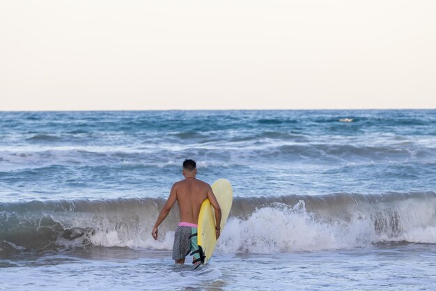 Man loopt de zee in met de surfplank.