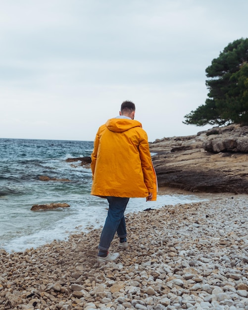 Man loopt langs rotsachtig strand in gele regenjas bewolkt winderig weer