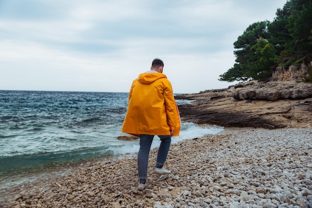 Man loopt langs rotsachtig strand in gele regenjas bewolkt winderig weer