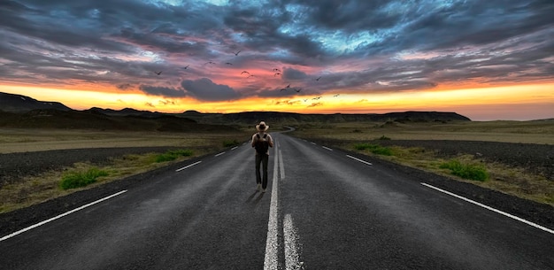 Man lopen op de weg en op de achtergrond een zonsondergang