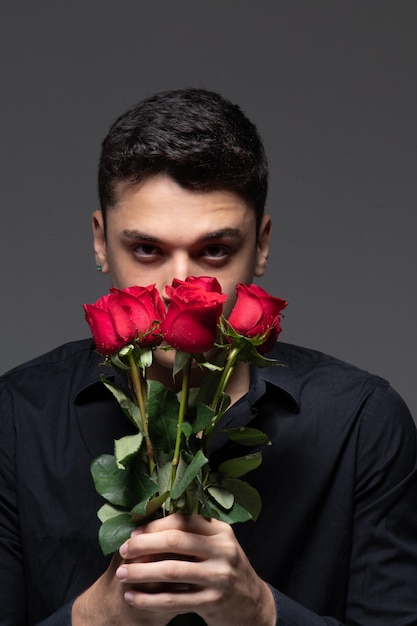 Uomo innamorato che indossa abiti scuri con in mano un mazzo di rose rosse foto in studio sfondo grigio