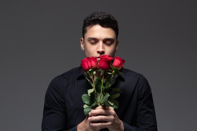 man in love wearing dark clothes holding a bouquet of red roses photo in studio gray background