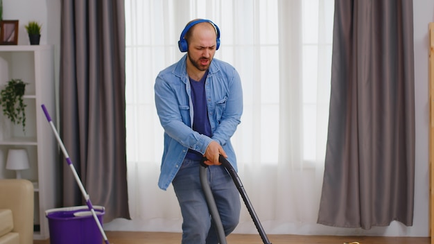 Man luistert muziek op hoofdtelefoon terwijl hij het appartement op de vloer schoonmaakt met stofzuiger