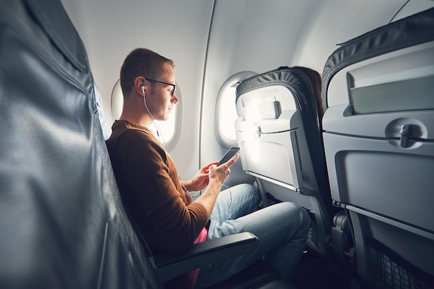 Man luistert naar muziek terwijl hij met zijn mobiele telefoon in het vliegtuig rijdt